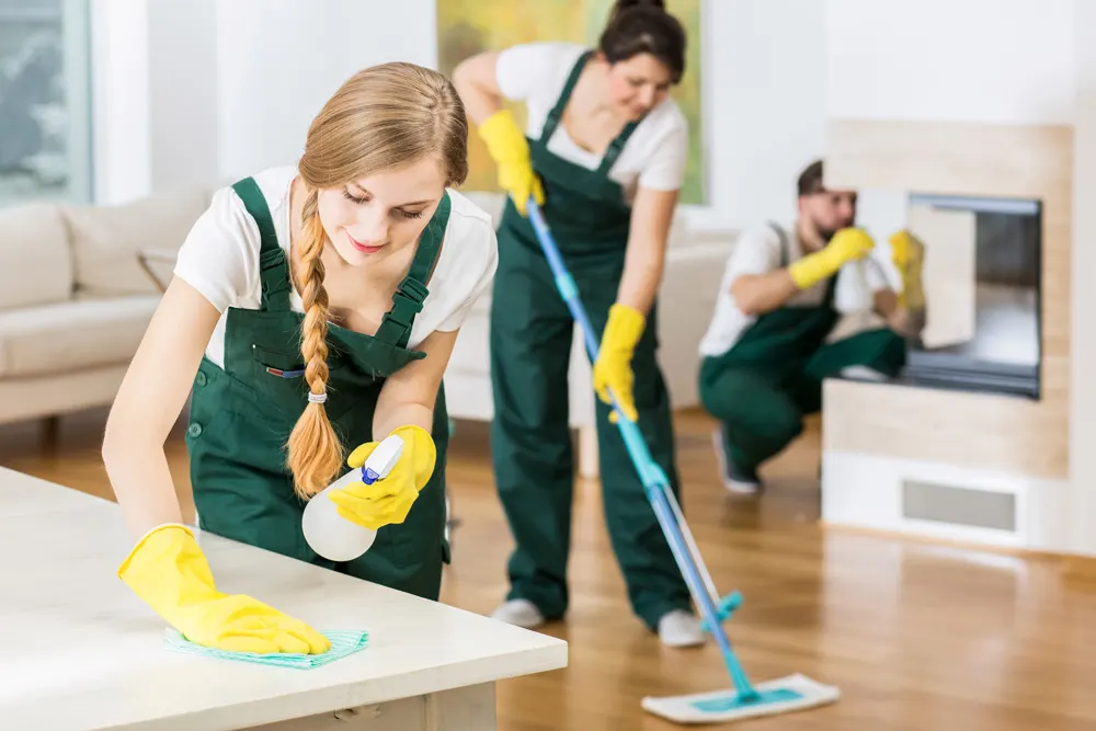 Residential cleaning service team in matching branded uniforms cleaning bright modern home interior with vacuum and cleaning supplies, representing reliable and trustworthy recurring cleaning services for TV advertising campaigns.
