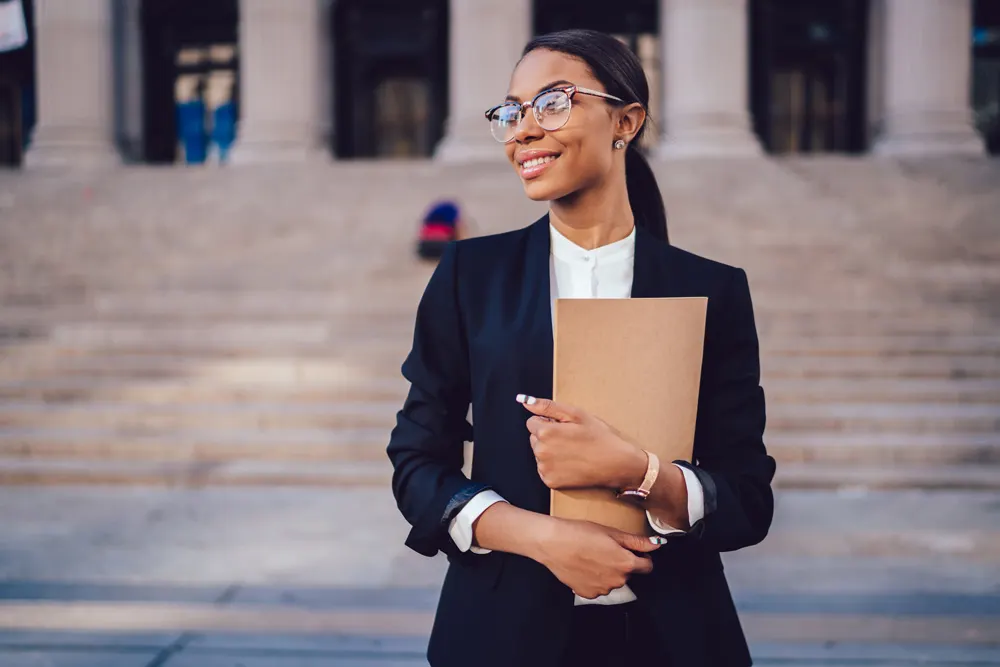 Experienced attorney in business suit standing confidently in modern law office with extensive legal book collection, representing credible legal representation for personal injury, family law, criminal defense, and estate planning TV advertising.